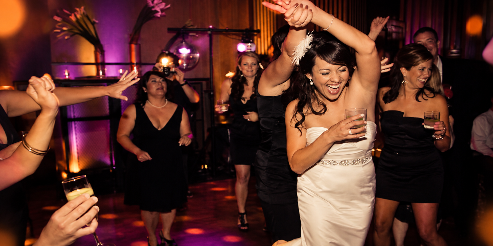 A bride dancing with her arms up on a packed floor
