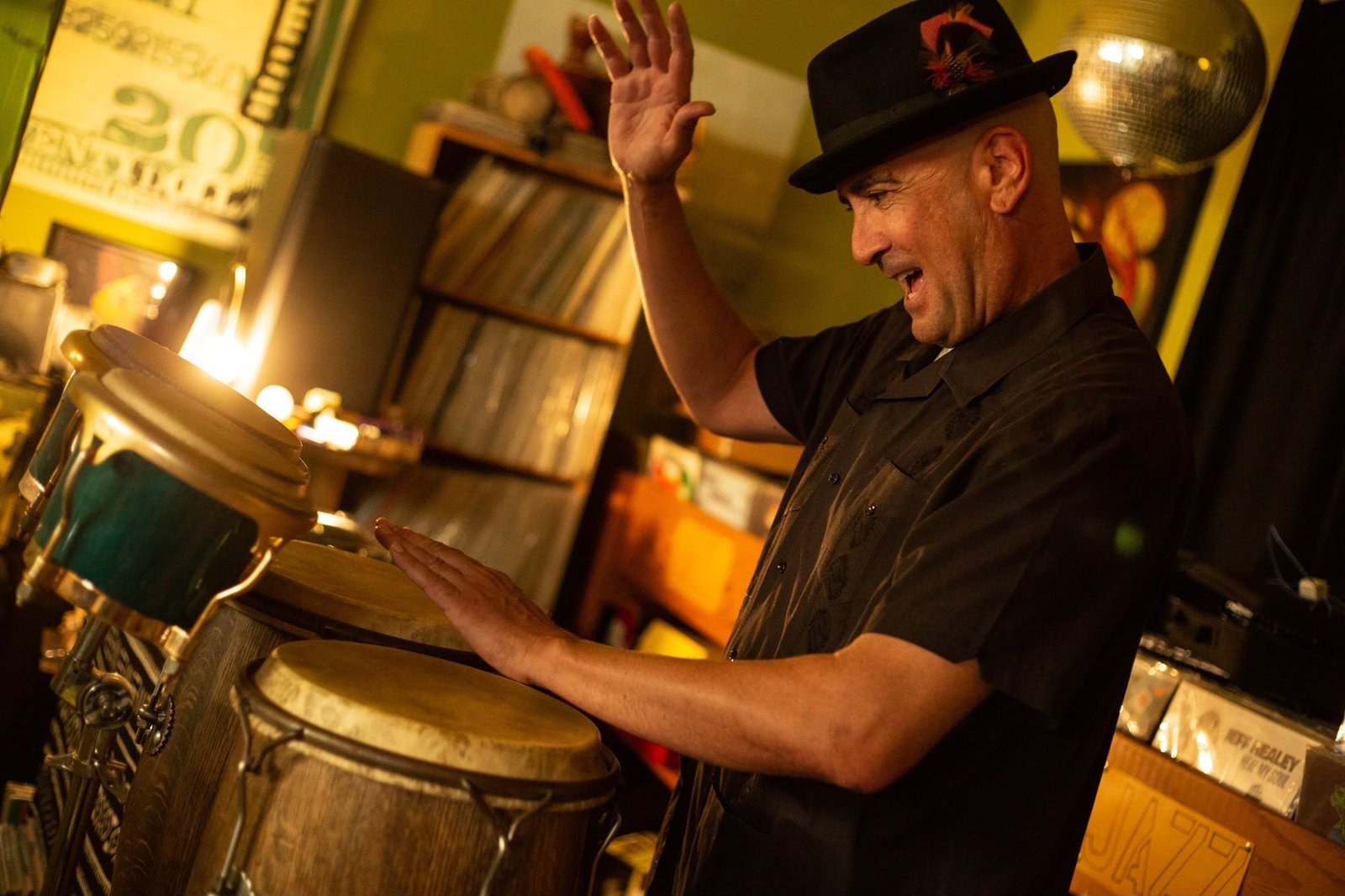 Goyo playing congas beside his record shelves